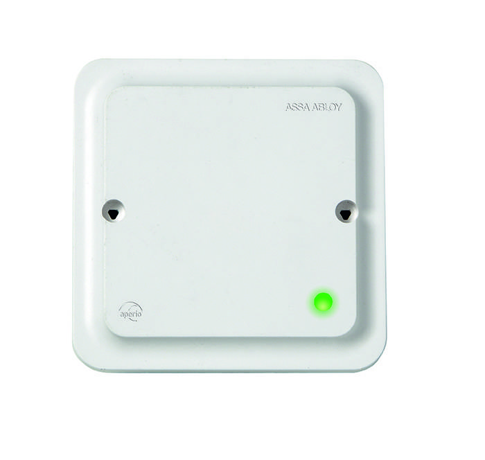 Ein weißes, wandmontiertes Gerät mit einer grünen Statusanzeige, das die Markenlogos von 'ASSA ABLOY' und 'aperio' trägt.