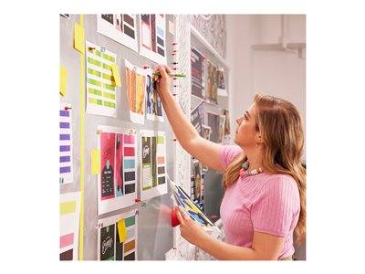 Eine Frau begutachtet bunte Designentwürfe, die an einer Wand in einem Büro angeheftet sind, was auf eine kreative Brainstorming- oder Feedbacksitzung hindeutet.