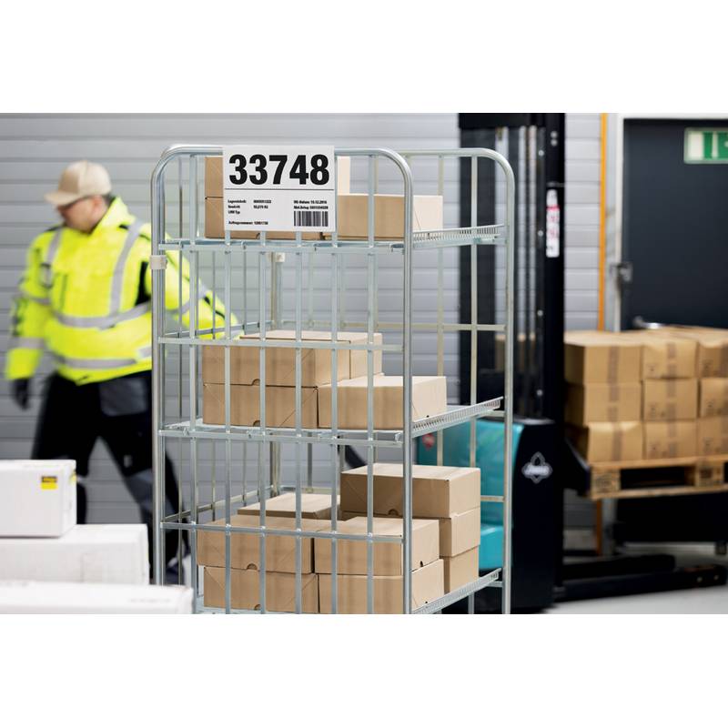 Ein Arbeiter in einer Sicherheitsweste bewegt kleine Kisten auf einem Metallwagen mit der Beschriftung 