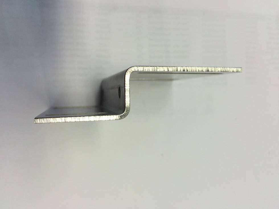 Seitenansichtfoto einer gebogenen Metallhalterung mit zwei horizontalen Flanschen und einer zentralen Versatzstute auf hellem Hintergrund.