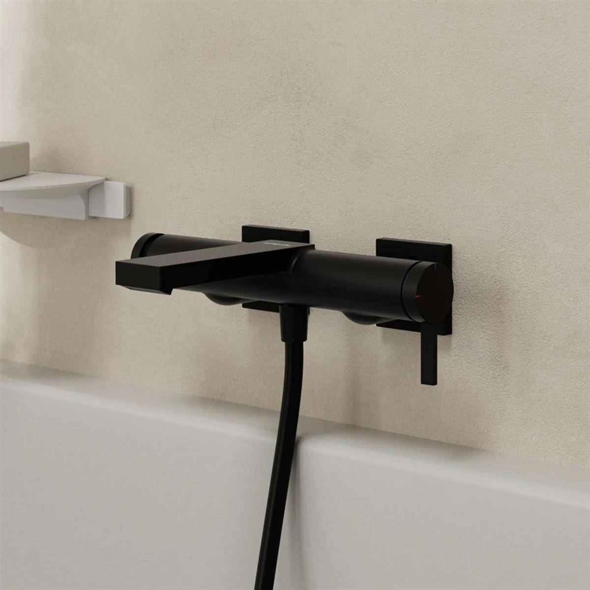 Schwarzer wandmontierter Badewannenmischer mit tragbarem Duschschlauch, über einer Badewanne an einer beigen Wand installiert.