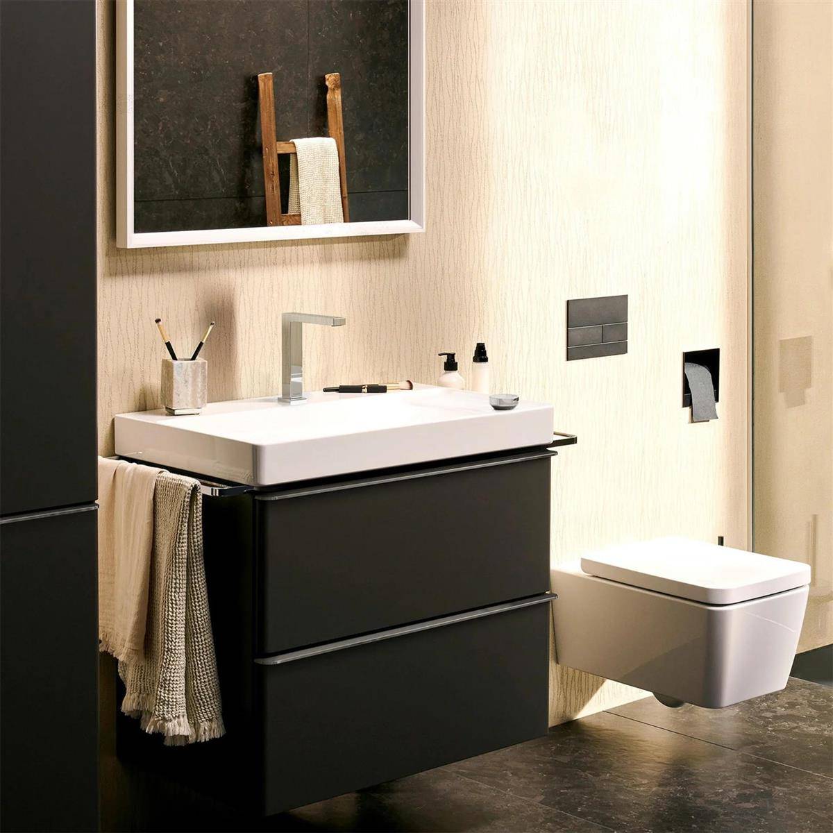 Modernes Badezimmer mit an der Wand montiertem Toilettensitz neben einem dunklen Waschtisch und Waschbecken, beleuchtet durch einen Spiegel und neutrale Wandfliesen.