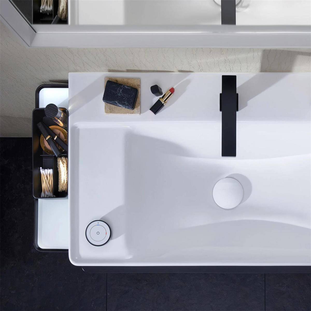 Draufsicht auf ein modernes Badezimmerbecken mit schwarzem Wasserhahn, Seife, Lippenstift und einem Seitentablett, das Schminkpinsel und Wattestäbchen hält.