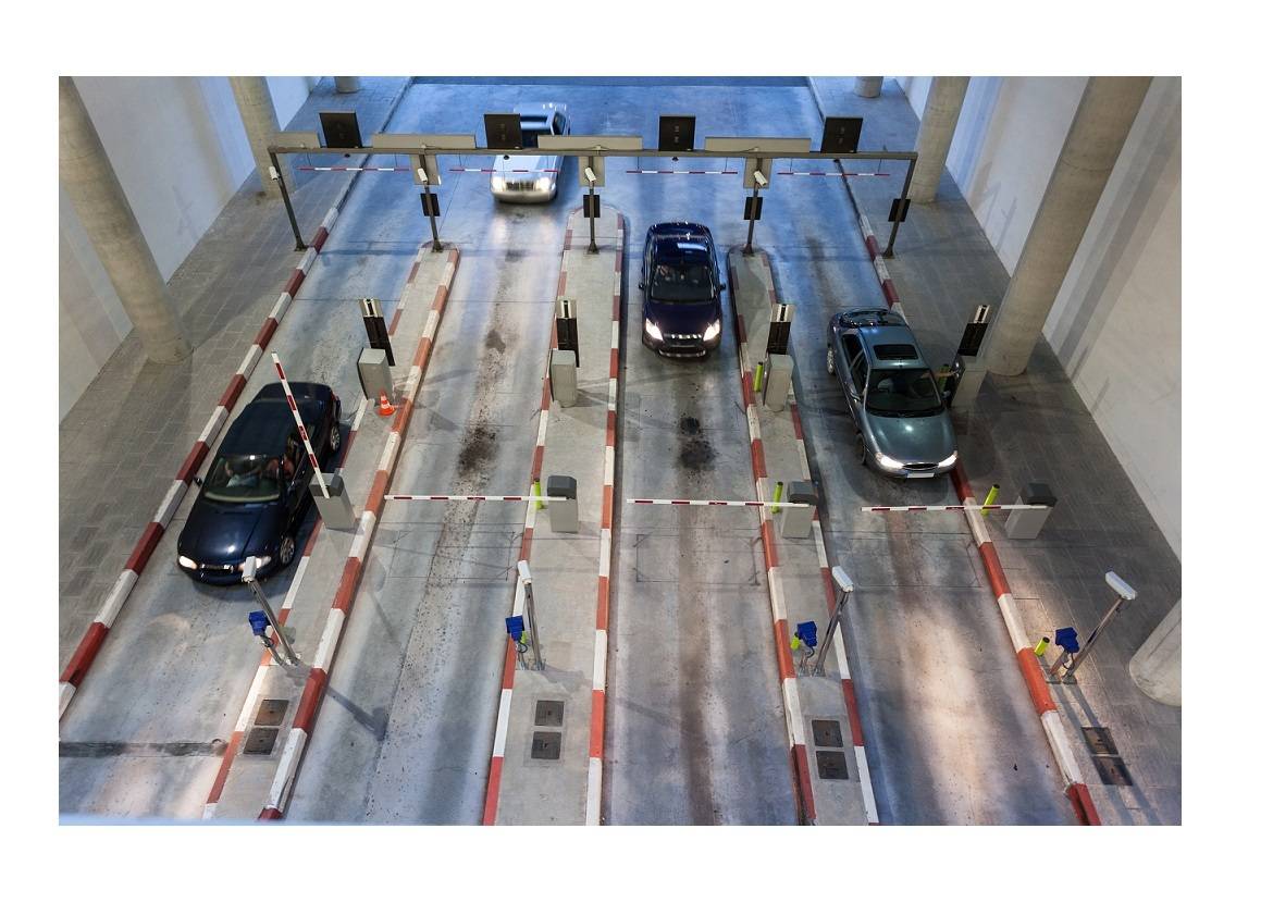 Vier Autos fahren durch eine Mautstelle mit mehreren Fahrspuren und Schranken, von oben betrachtet.