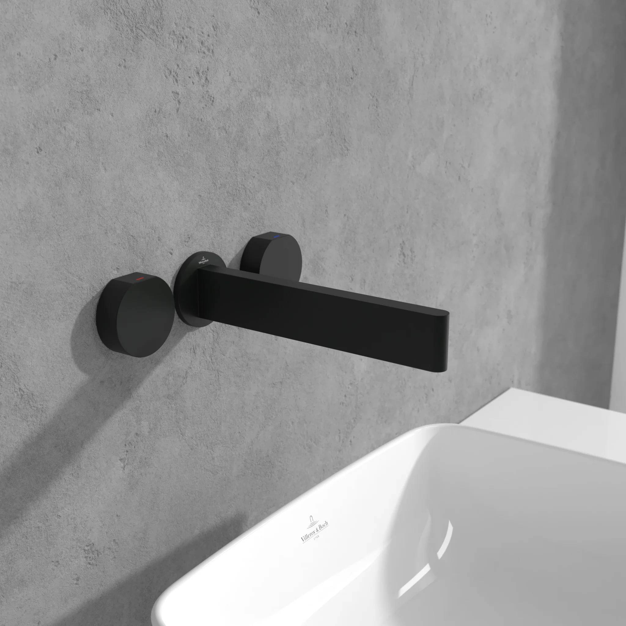Wandmontierter matter schwarzer Wasserhahn über einem weißen rechteckigen Waschbecken an einer grauen Betonwand.