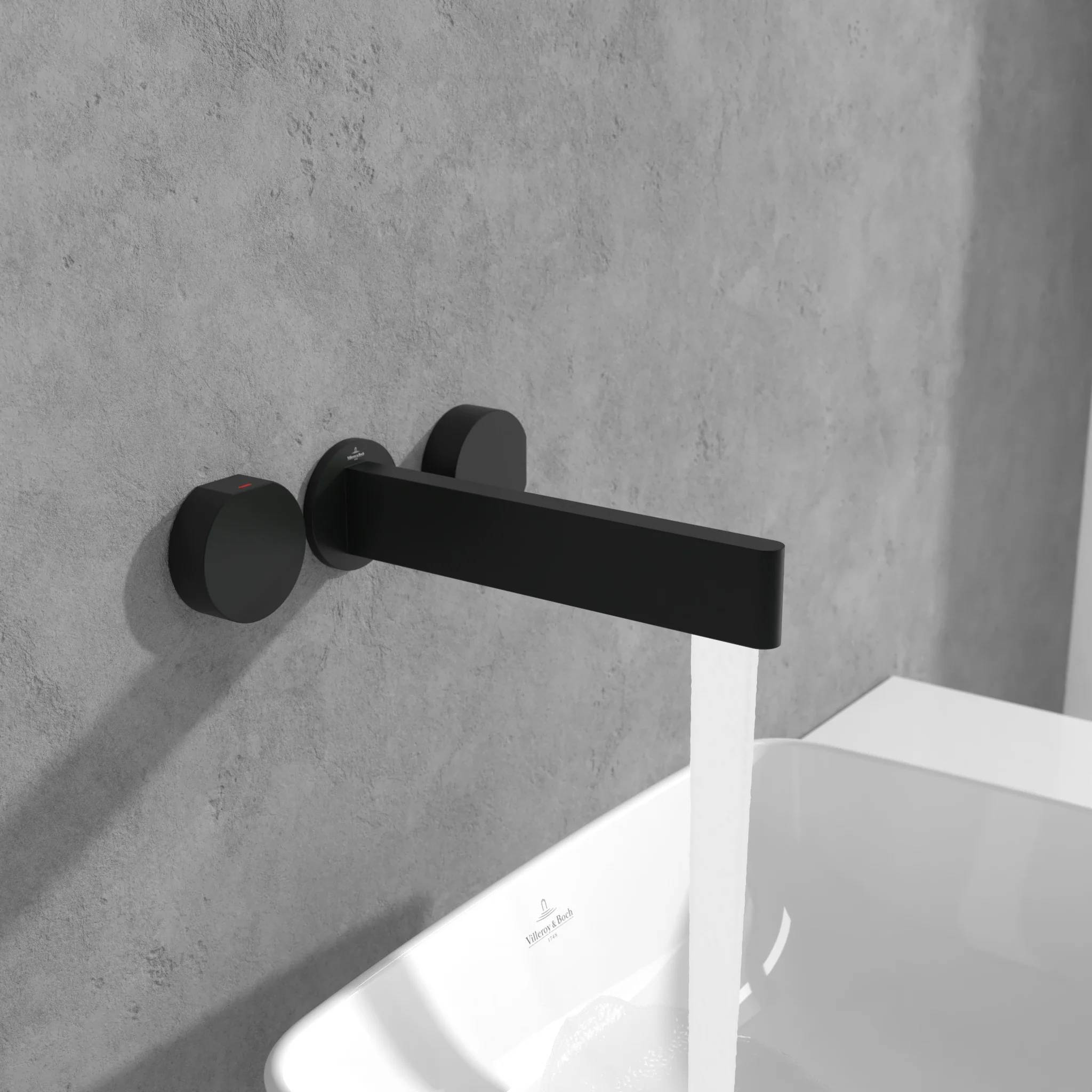 Moderner schwarzer an der Wand montierter Wasserhahn, der ein weißes Waschbecken vor einer grauen Betonwand füllt.