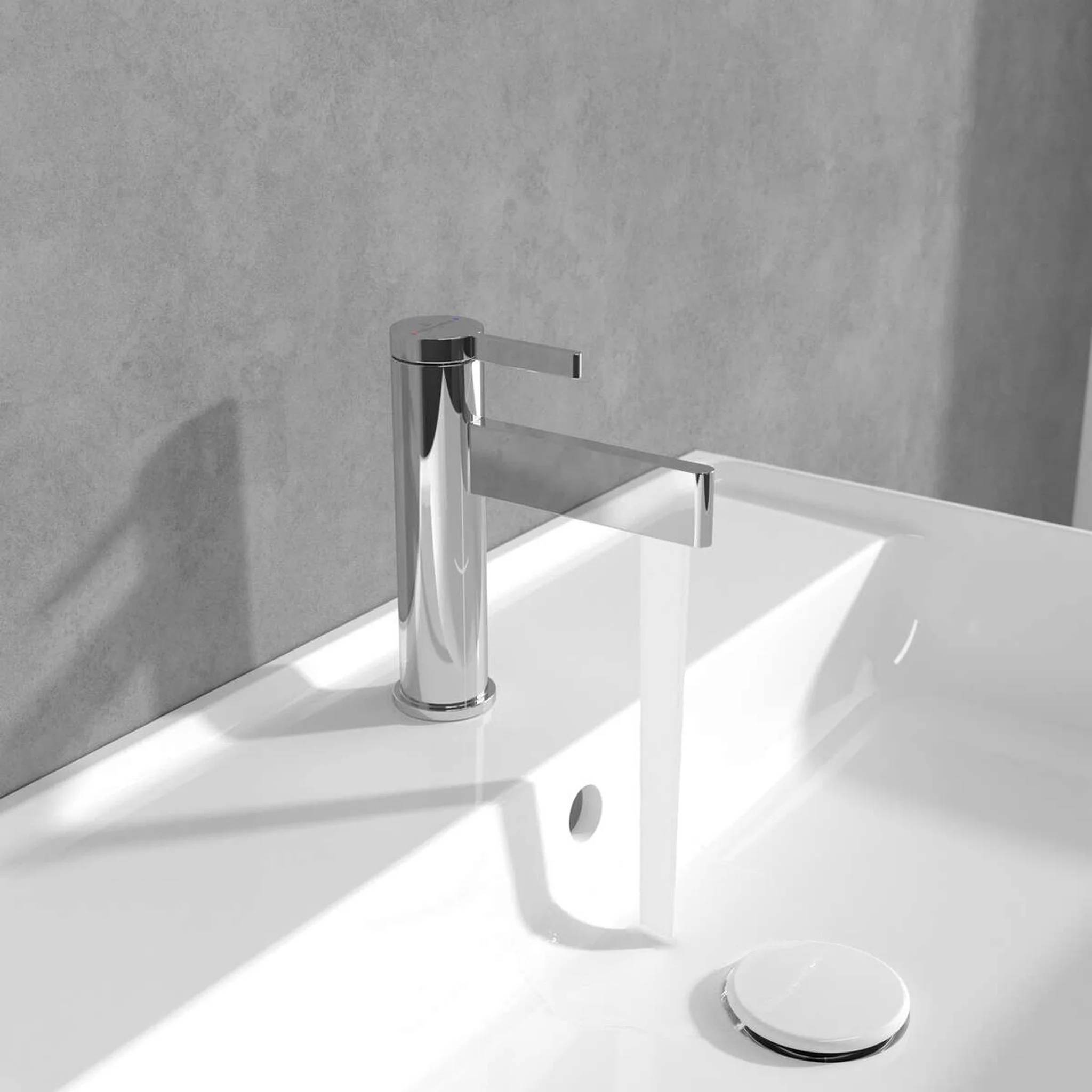 Moderner Chrom-Badezimmerhahn über einem weißen Waschbecken mit integriertem Überlaufloch und Ablaufstöpsel vor einer grauen Wand.