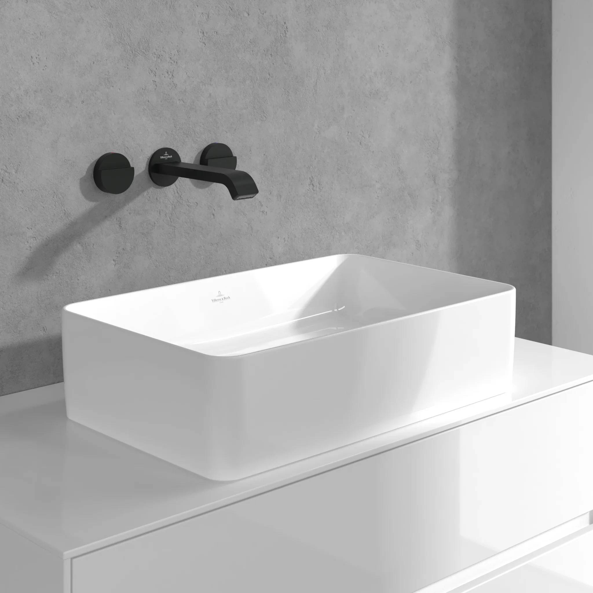Modernes weißes rechteckiges Waschbecken auf einem Waschtisch mit schwarzer wandmontierter Armatur vor einer grau gefliesten Badezimmerwand.