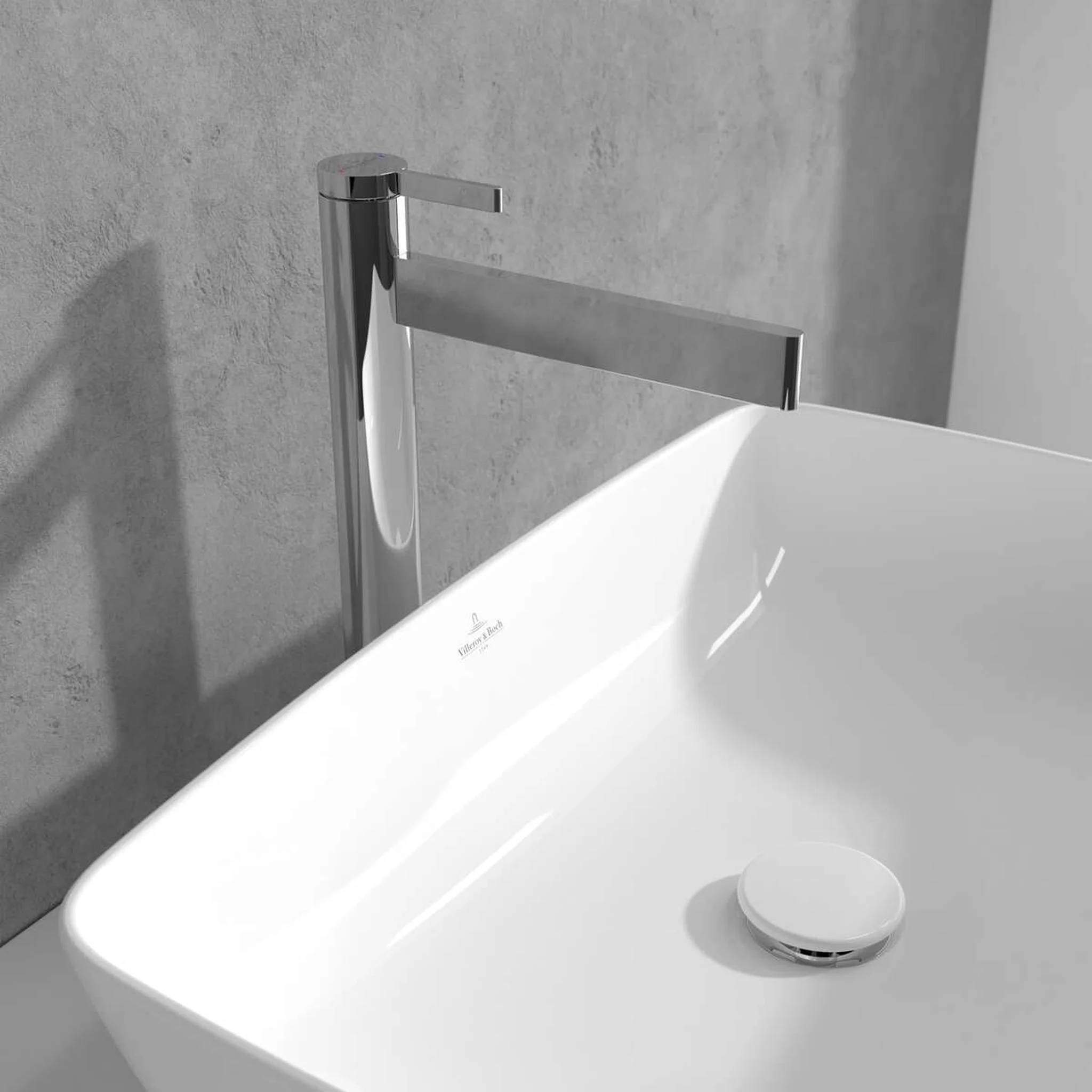 Minimalistische weiße Badewanne mit wandmontiertem Chromhahn und Überlaufventil vor einer grauen Wand.
