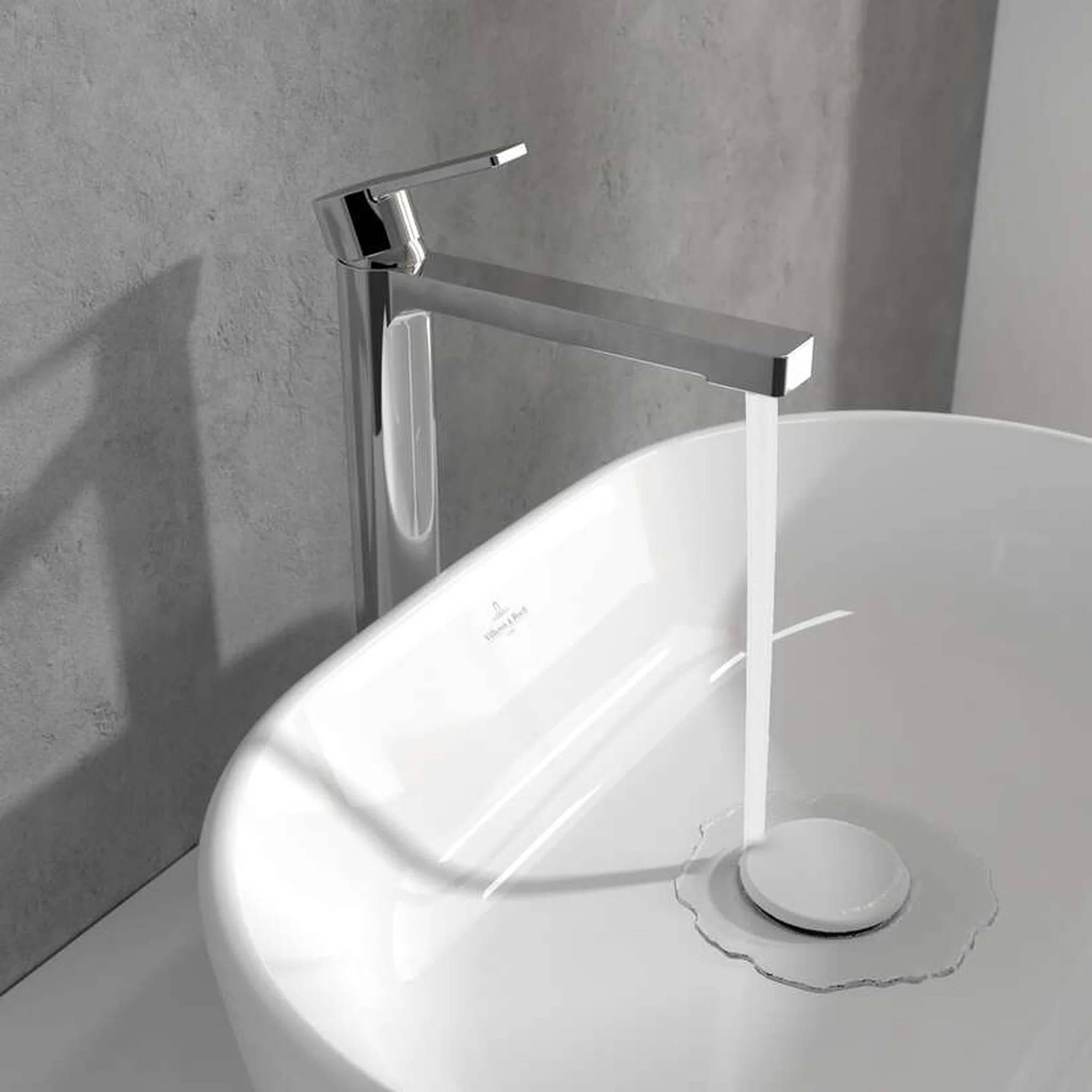 Moderner Chromwasserhahn, der in ein weißes Aufsatzwaschbecken an einer grauen Wand läuft, mit Wasser, das in den Abfluss fließt.