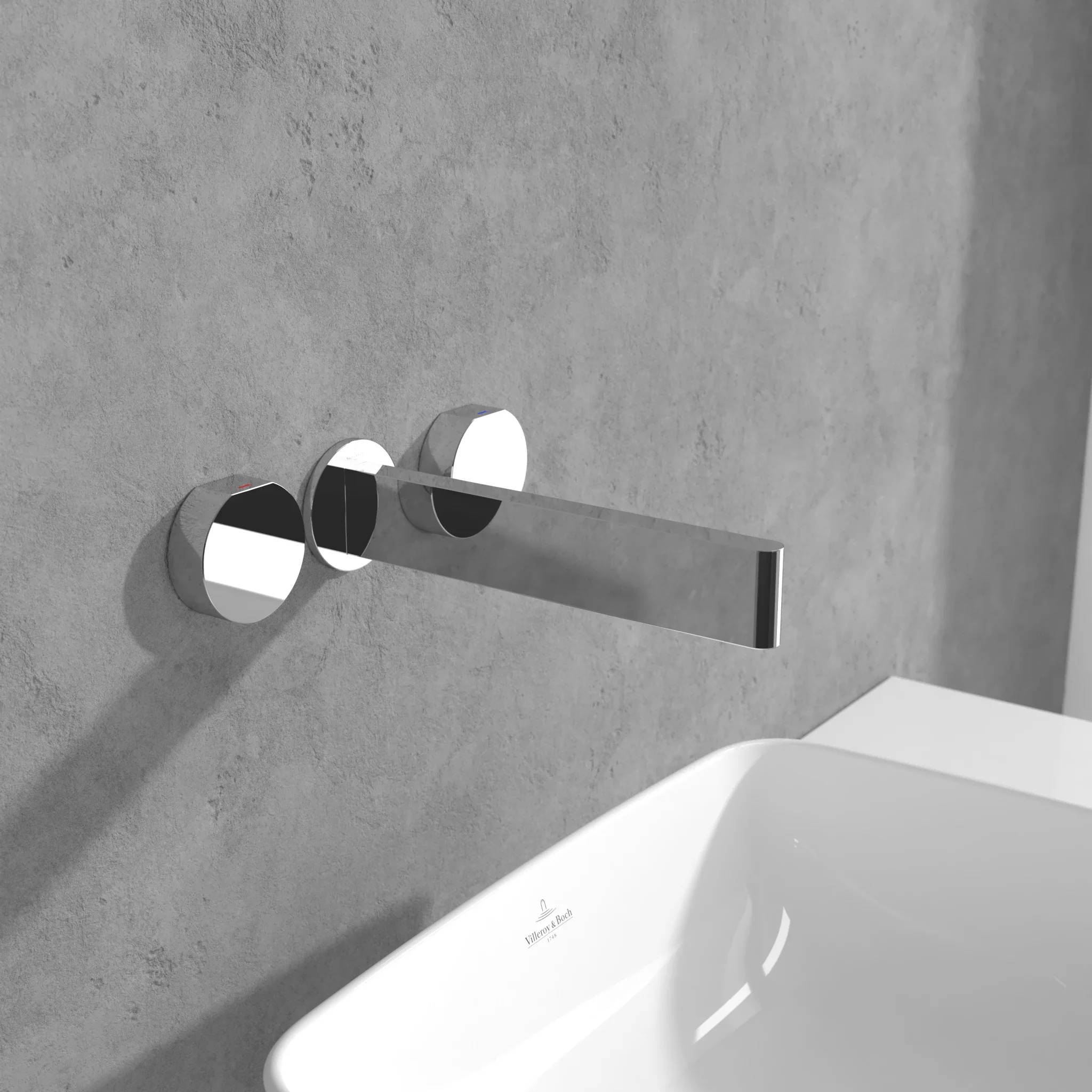 Moderner, an der Wand montierter Chromwasserhahn über einem weißen Waschbecken vor einer grauen Betonwand.