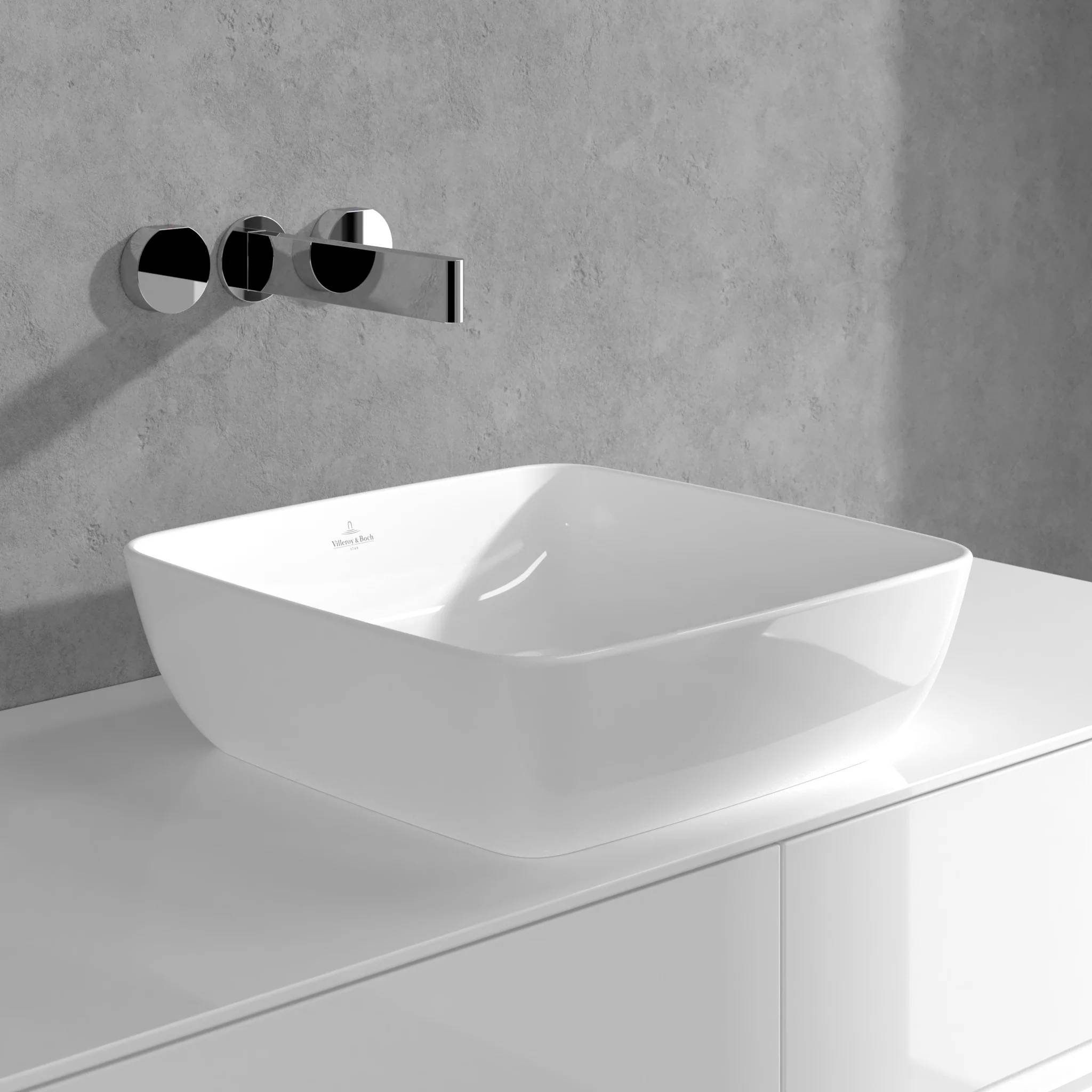 Modernes weißes Waschbecken mit quadratischer Form auf einer Badezimmerablage mit wandmontiertem Chromwasserhahn vor einer grauen Wand.