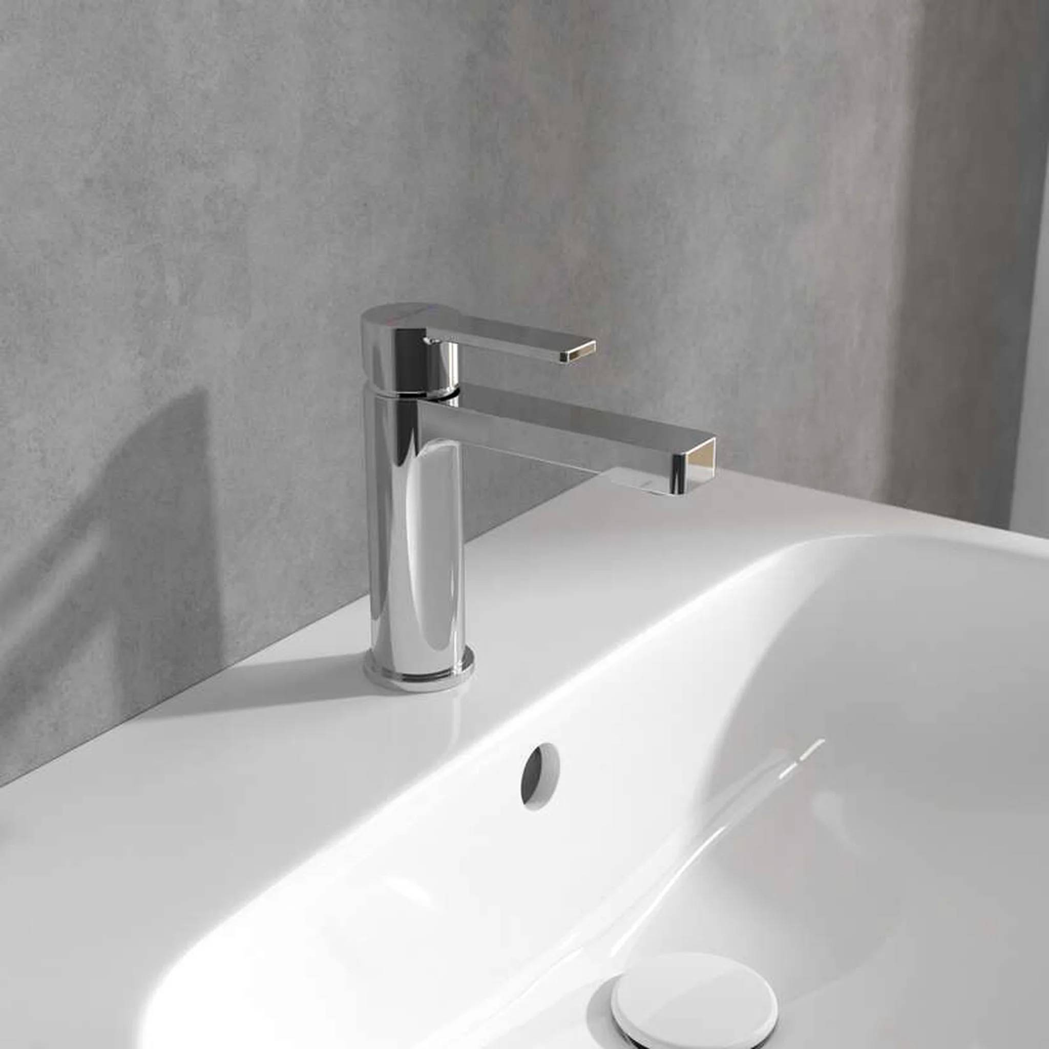 Chrom-Badezimmerwasserhahn über einem weißen Waschbecken an einer grauen Wand, mit einem runden Abflussloch, das im Waschbecken sichtbar ist.