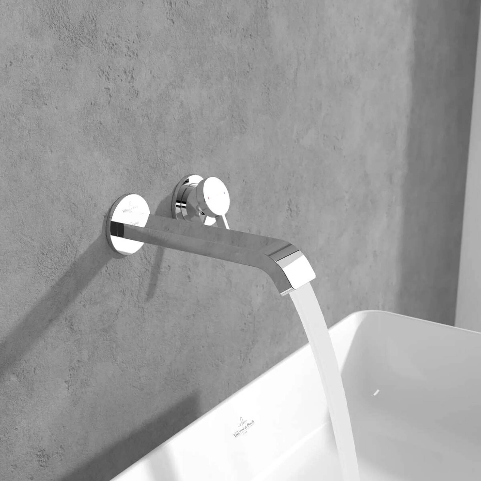 Wandmontierter Badewannenmischer aus Chrom mit Wasser, das in eine weiße Wanne gegen eine graue Wand fließt.