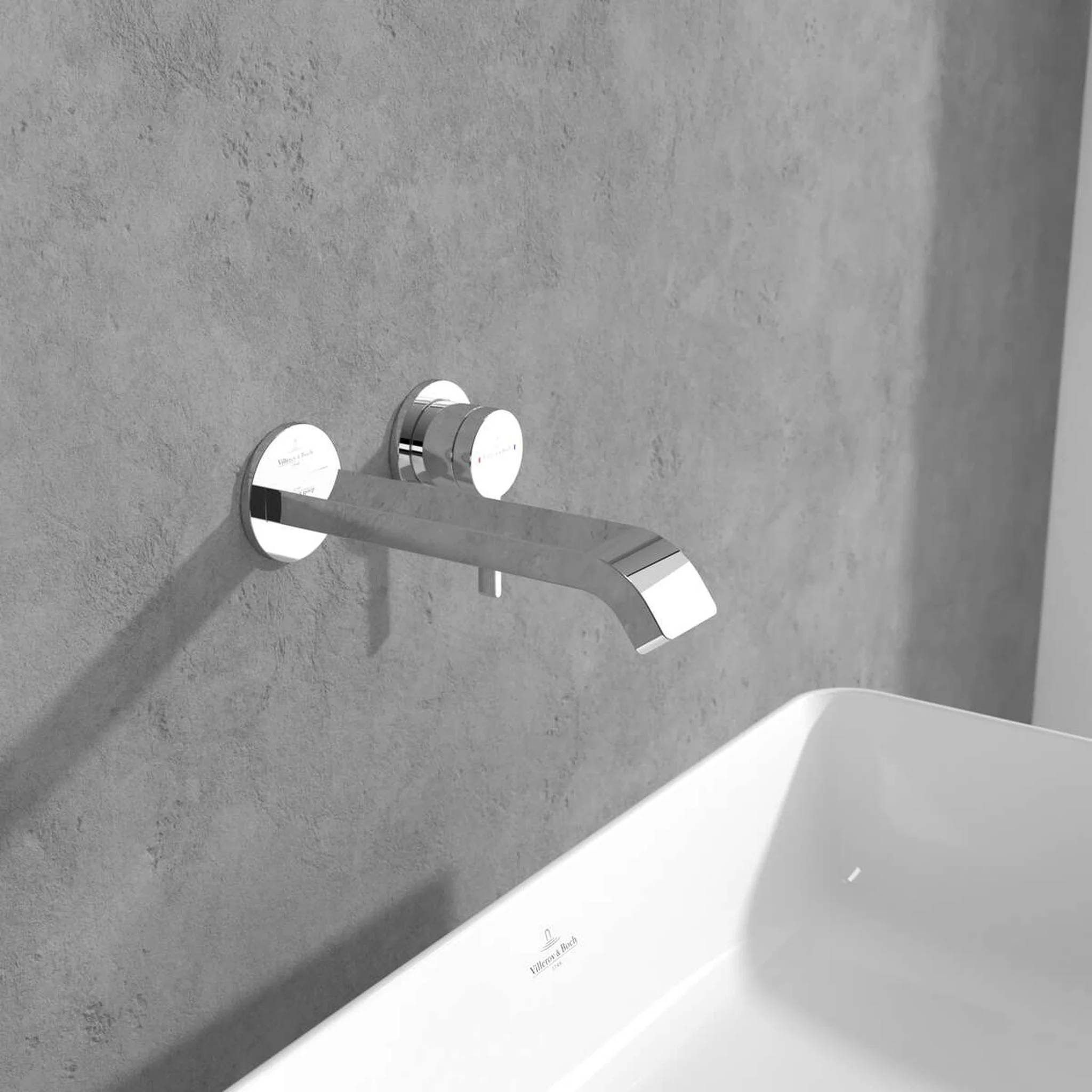 Moderner verchromter Wandmontage-Badewannenmischer über einer weißen Badewanne an einer grauen Betonwand.