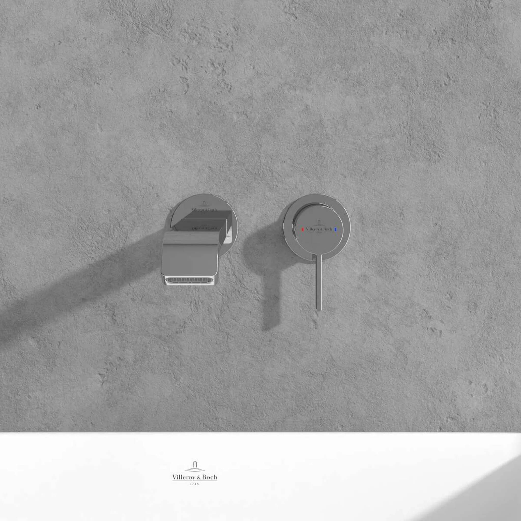 Minimalistische Wandarmatur mit kreisförmigem Stellhebel an einer grauen Betonwand über einem weißen Waschbecken, mit Villeroy & Boch-Branding darunter.