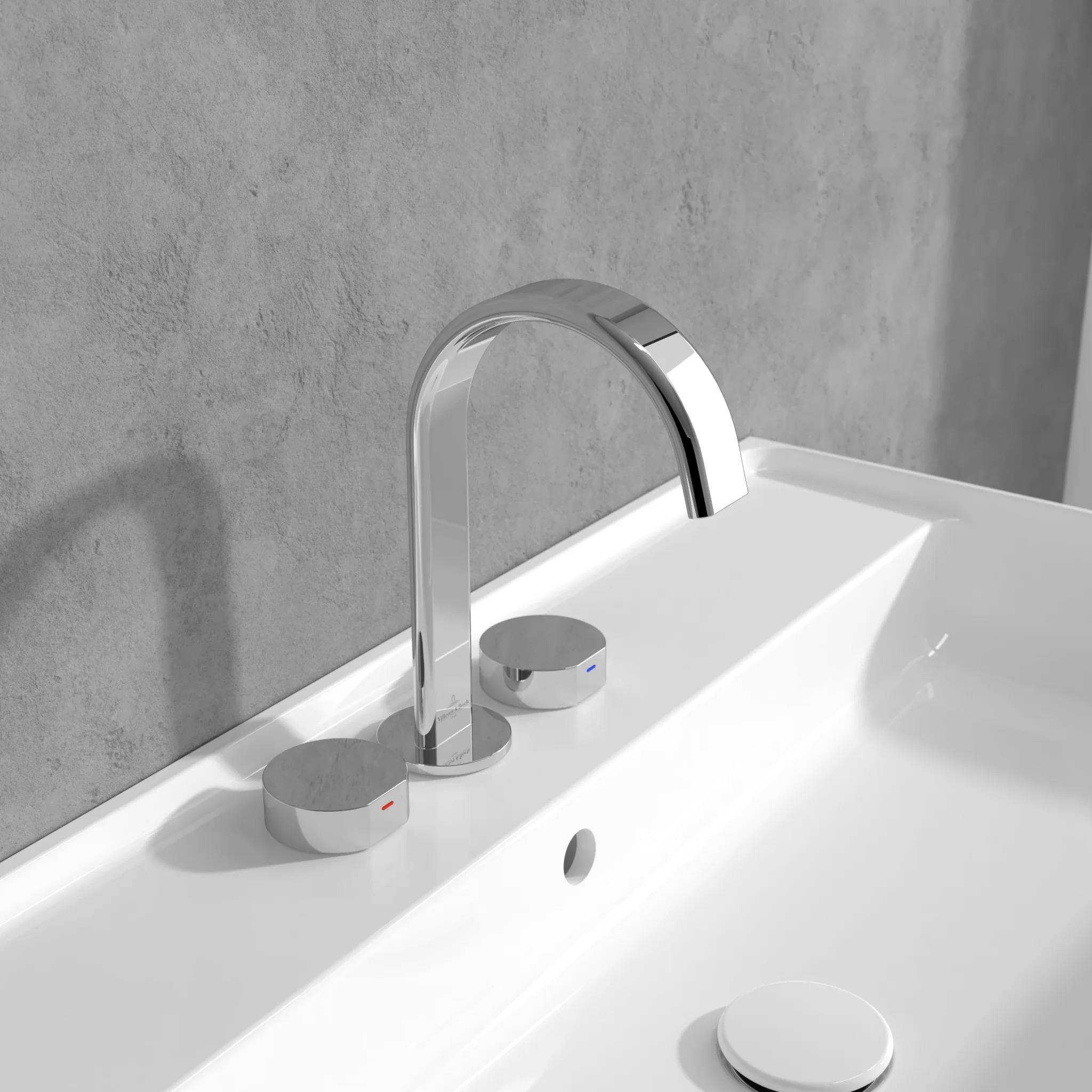 Moderner Badezimmerwasserhahn aus Chrom mit zwei runden Bedienungsknöpfen, montiert auf einem weißen Waschbecken vor einer grauen Wand.