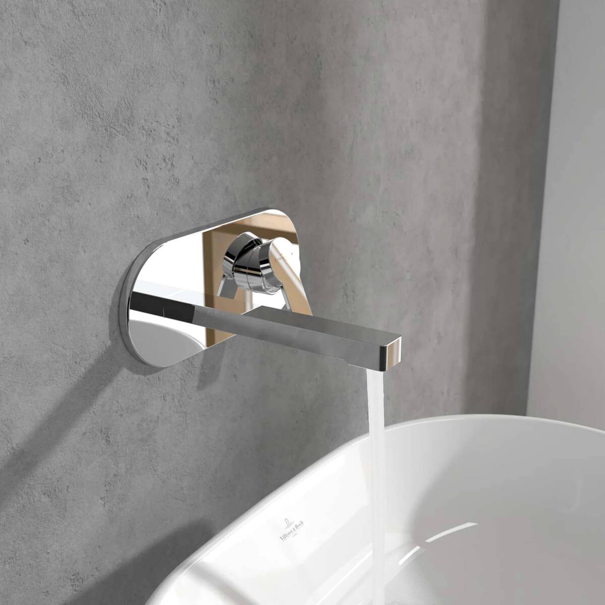 Moderner wandmontierter Chromwasserhahn, der eine weiße Badewanne gegen eine graufliesige Wand füllt.