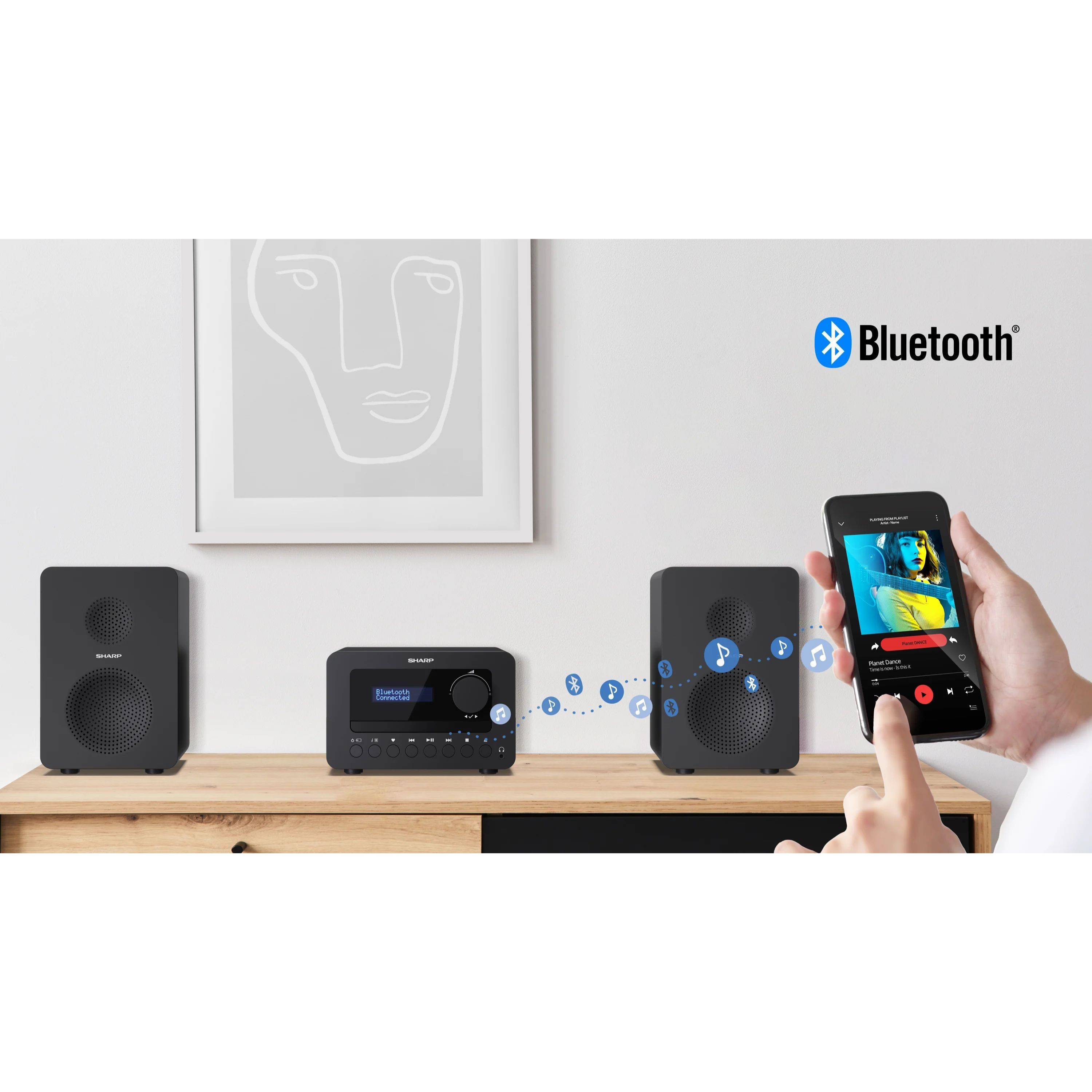 Hände, die ein Smartphone halten, das Musik via Bluetooth an eine kompakte Heimstereoanlage mit zwei Lautsprechern und einem Receiver auf einem Regal streamt.