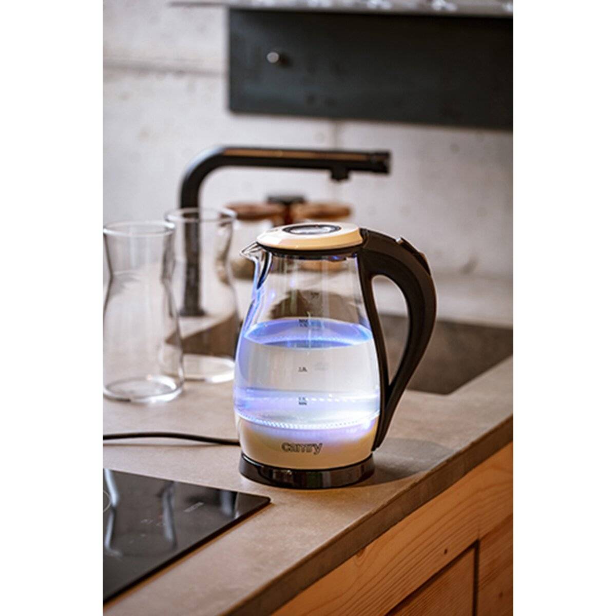 Ein gläserner Elektrokessel leuchtet blau auf einer Küchentheke, neben einem Wasserhahn und Gläsern, was anzeigt, dass er eingeschaltet ist und Wasser erhitzt.