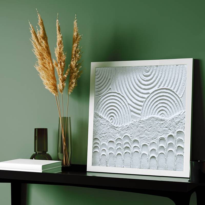 Ein modernes Kunstwerk mit konzentrischen Mustern neben einer Vase mit getrockneten Pflanzen auf einem Regal vor einer grünen Wand.