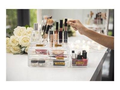 Make-up-Organizer mit Lippenstift, Pinseln und Nagellack auf einem Schminktisch. Eine Hand greift nach einem Lippenstift. Rosen und Lichter im Hintergrund.