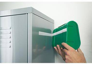 Eine Hand platziert einen grünen Behälter gegen einen Metallschrank oder ein Haushaltsgerät mit einem weißen Streifen oder einer weißen Halterung.