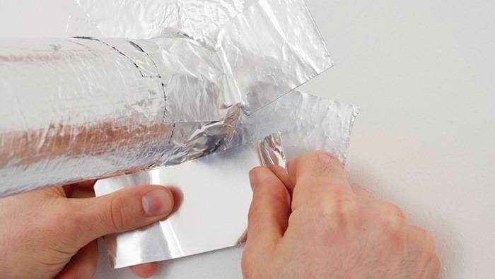 Eine Person, die ein Stück glänzende, reflektierende Aluminiumfolie abrollt, möglicherweise zur Verwendung beim Einwickeln oder Abdecken von Gegenständen.