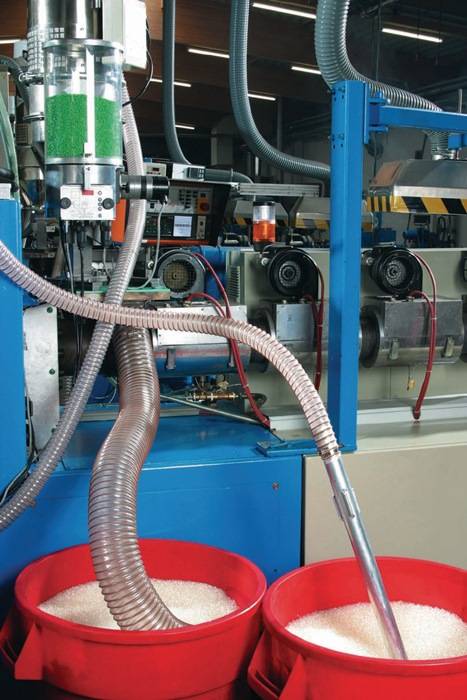 Eine Nahaufnahme von industrieller Maschinerie in einer Fabrikumgebung, die miteinander verbundene Metallrohre und Schalttafeln zeigt und einen Fertigungsprozess andeutet.