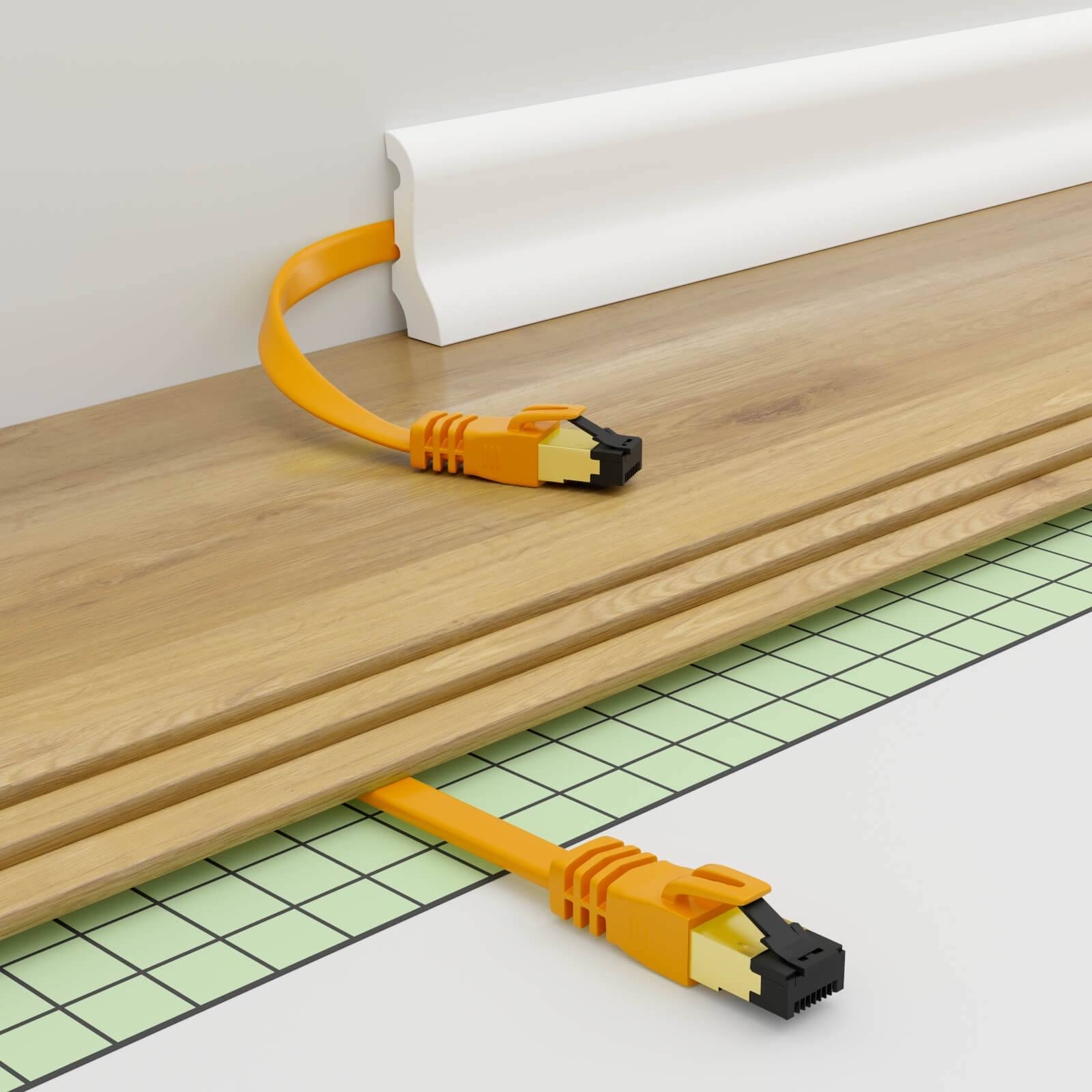 Oranges Ethernet-Kabel durch eine weiße Sockelleiste geführt und unter einem Holzbrett hervorkommend, zeigt verborgene Kabelführung.