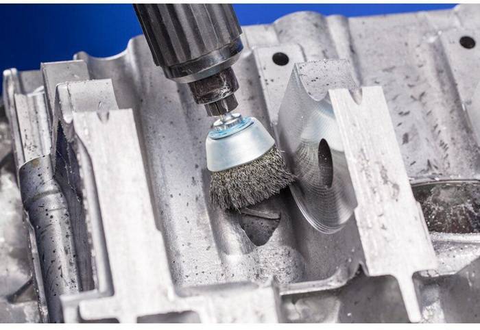 Ein Rotationswerkzeug mit einem Drahtbürstenaufsatz poliert eine Metalloberfläche und glättet raue Kanten sowie entfernt Ablagerungen, Nahaufnahme.