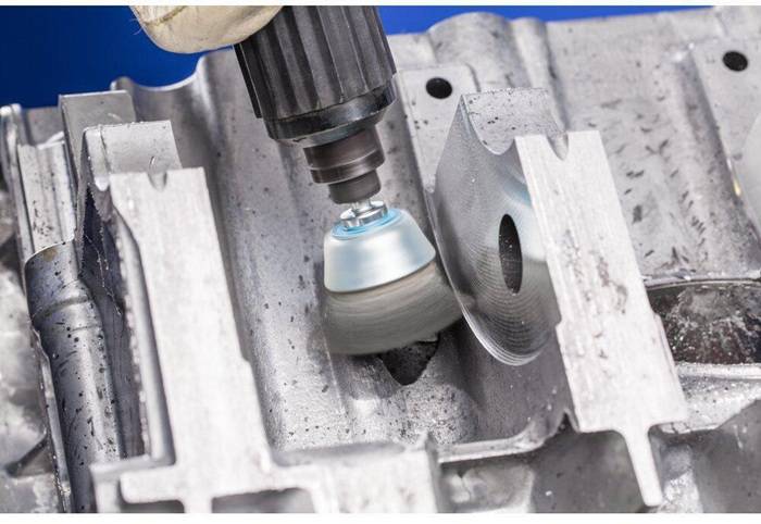 Ein Metallschleifwerkzeug im Einsatz, das ein Stück industrieller Metallmaschinerie glättet und einen Prozess andeutet, der wahrscheinlich mit Fertigung oder Reparatur zu tun hat.