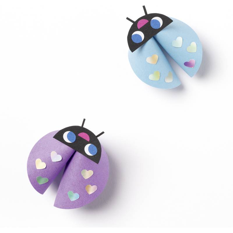 Zwei bunte Marienkäfer aus Papier, einer blau und einer lila, jeweils mit herzförmigen Punkten und schwarzen Köpfen. Sie scheinen zur Dekoration gebastelt worden zu sein.