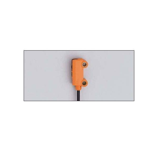 Ein orangefarbener Näherungssensor mit einem schwarzen Kabel ist an einer weißen Oberfläche befestigt.