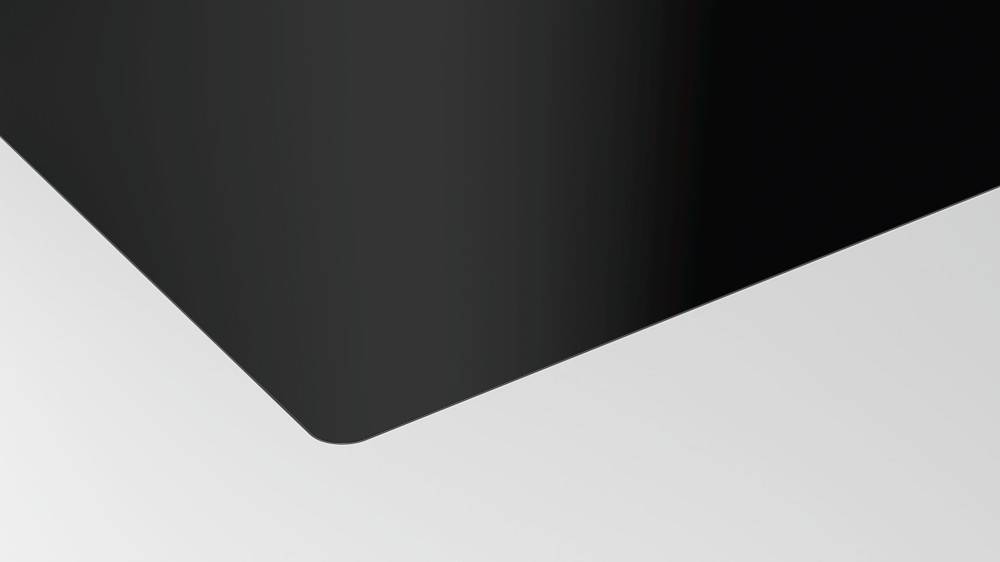 Eine Nahaufnahme der Ecke eines Laptops, die seinen schwarzen Metallic-Finish und seine abgerundete Kante vor einem hellgrauen Hintergrund zeigt.