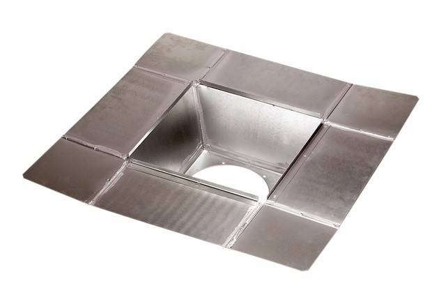 Ein metallener quadratischer Duschablaufdeckel mit einer zentralen quadratischen Öffnung für den Wasserablauf.