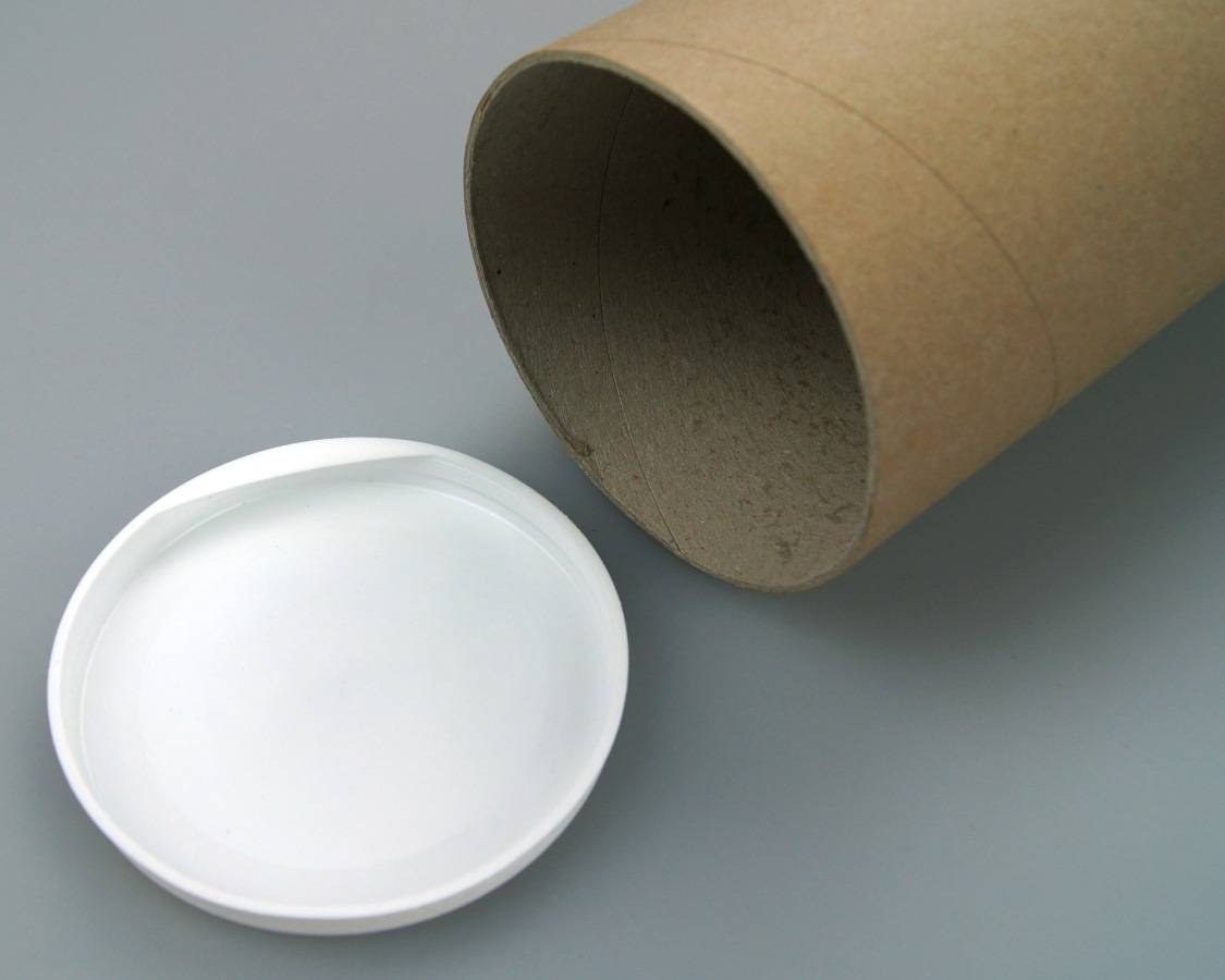 Eine braune Pappröhre mit einer entfernten weißen Kunststoffkappe liegt auf einer grauen Oberfläche. Das Rohr wird aus einer angewinkelten Draufsicht gezeigt.