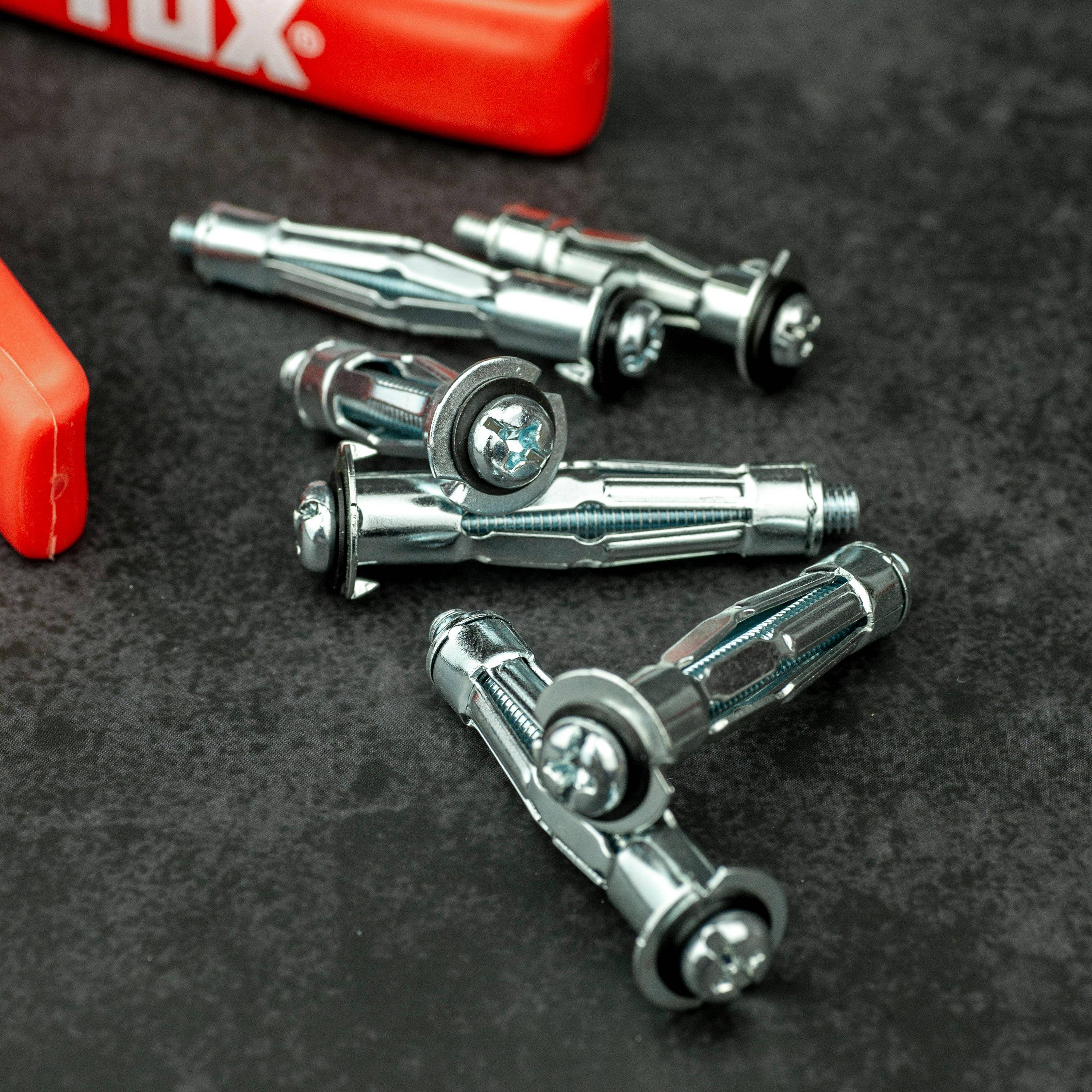 Metallwandanker mit Schraubköpfen sind auf einer dunklen Oberfläche neben einer teilweise sichtbaren roten Werkzeugkiste verstreut.