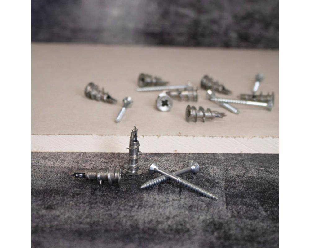 Metallschrauben verschiedener Größen, verstreut auf einer strukturierten Oberfläche, einige stehen aufrecht, andere liegen flach.