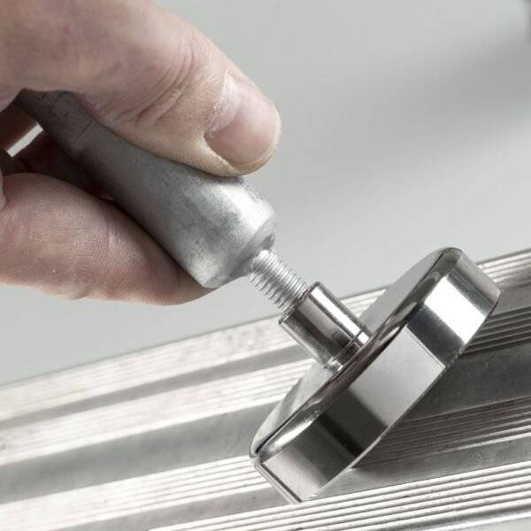 Nahaufnahme einer Hand, die ein Metallwerkzeug verwendet, um eine verchromte Armatur auf einer gerillten Metallfläche festzuziehen oder anzupassen.