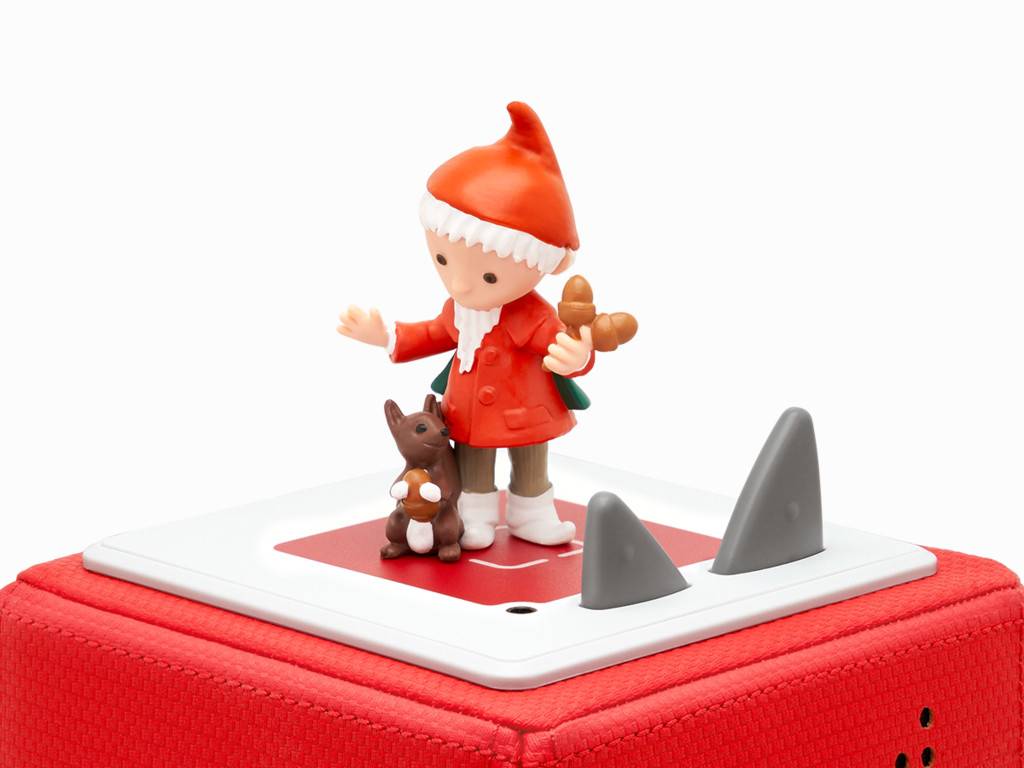 Eine kleine Weihnachtsmannfigur steht auf einer weißen Plattform mit einem brauen Tier und zwei grauen Spitzen auf einer roten strukturierten Schachtel.