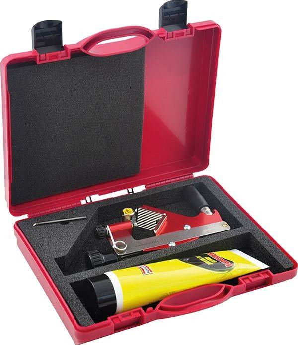 Ein roter Plastikkoffer, der einen Heißluftfön und eine gelbe Klebstoffröhre enthält, beide in schwarze Schaumstoffeinlagen eingebettet.