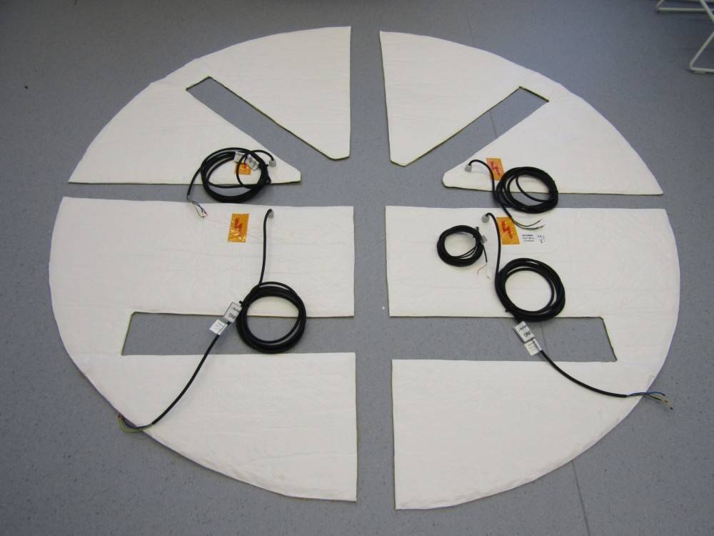 Kreisförmige Matte, die in sechs dreieckige Segmente geschnitten ist, mit fünf schwarzen Kabeln, die darauf gewickelt sind, auf einem grauen Boden angeordnet.