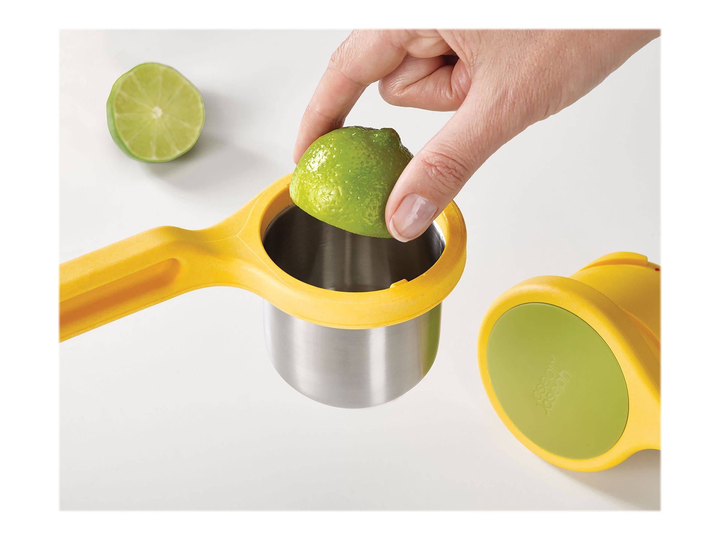 Eine Hand presst eine Limettenhälfte in einer gelben Zitronenpresse, während eine weitere Limettenhälfte daneben liegt.