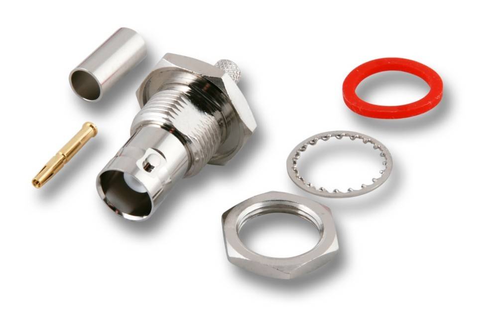 Ein zerlegter Koaxialstecker, der verschiedene Teile zeigt, darunter einen Metallzylinder, einen Ring und eine kleine rote Unterlegscheibe, auf einer weißen Oberfläche.