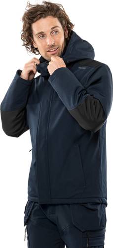 Eine Person schließt eine blaue Winterjacke zu und betont dabei Wärme und Komfort vor einem schwarzen Hintergrund.