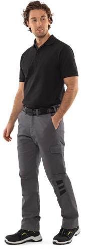 Eine Person mit einem schwarzen T-Shirt und grauen Cargohosen, die mit in den Taschen verschränkten Händen steht.