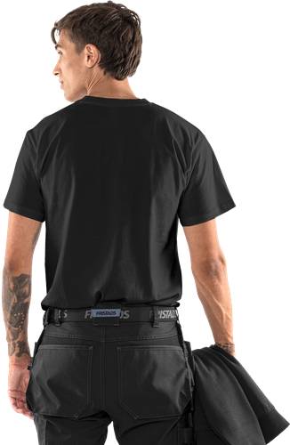 Eine Person mit kurzen Haaren trägt ein schwarzes Hemd und schwarze Hosen, von hinten gesehen. Ein Arm zeigt ein großes Tattoo.