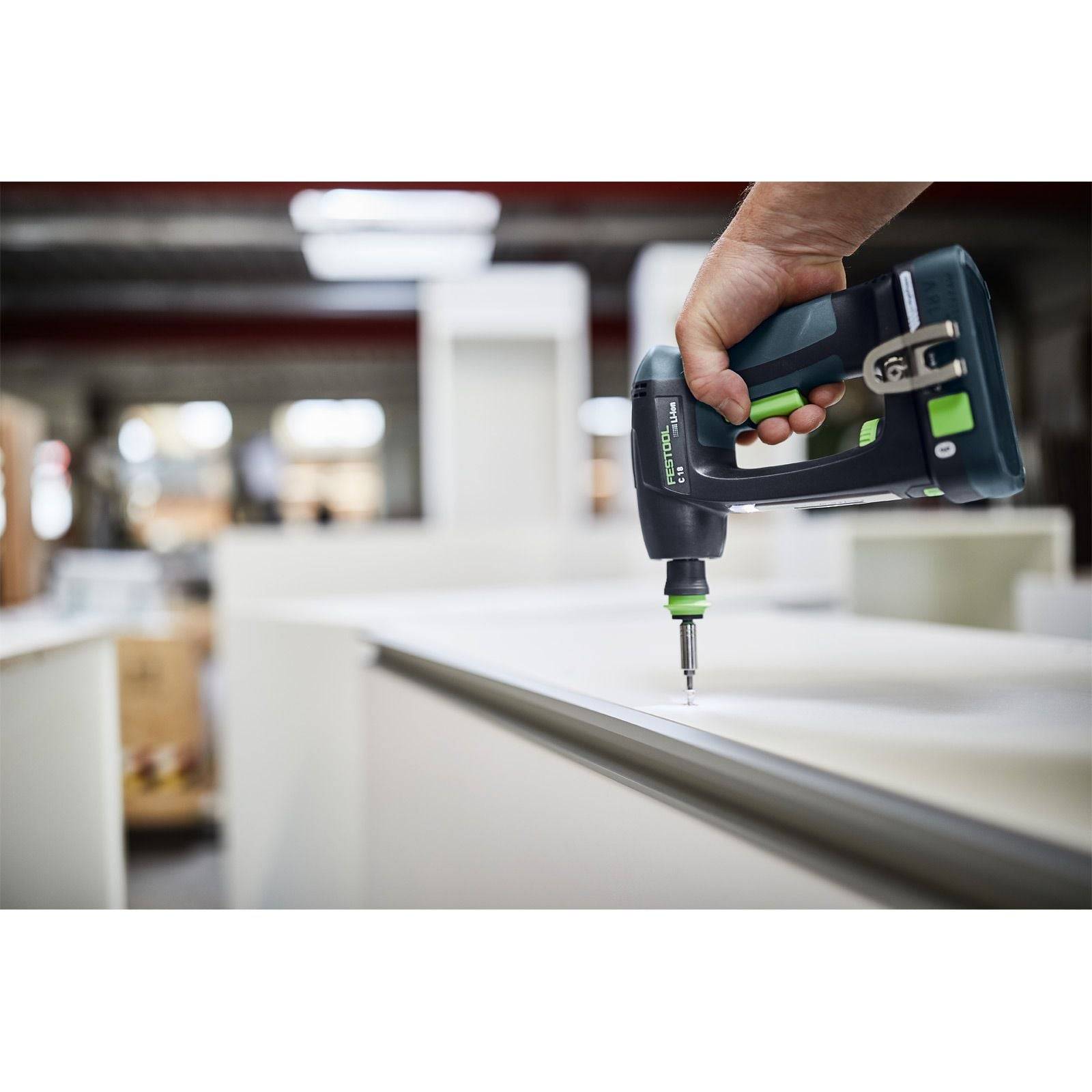 Eine Hand, die einen kabellosen elektrischen Schraubendreher verwendet, um eine Schraube in eine weiße Holzplatte in einer Werkstattumgebung zu befestigen.