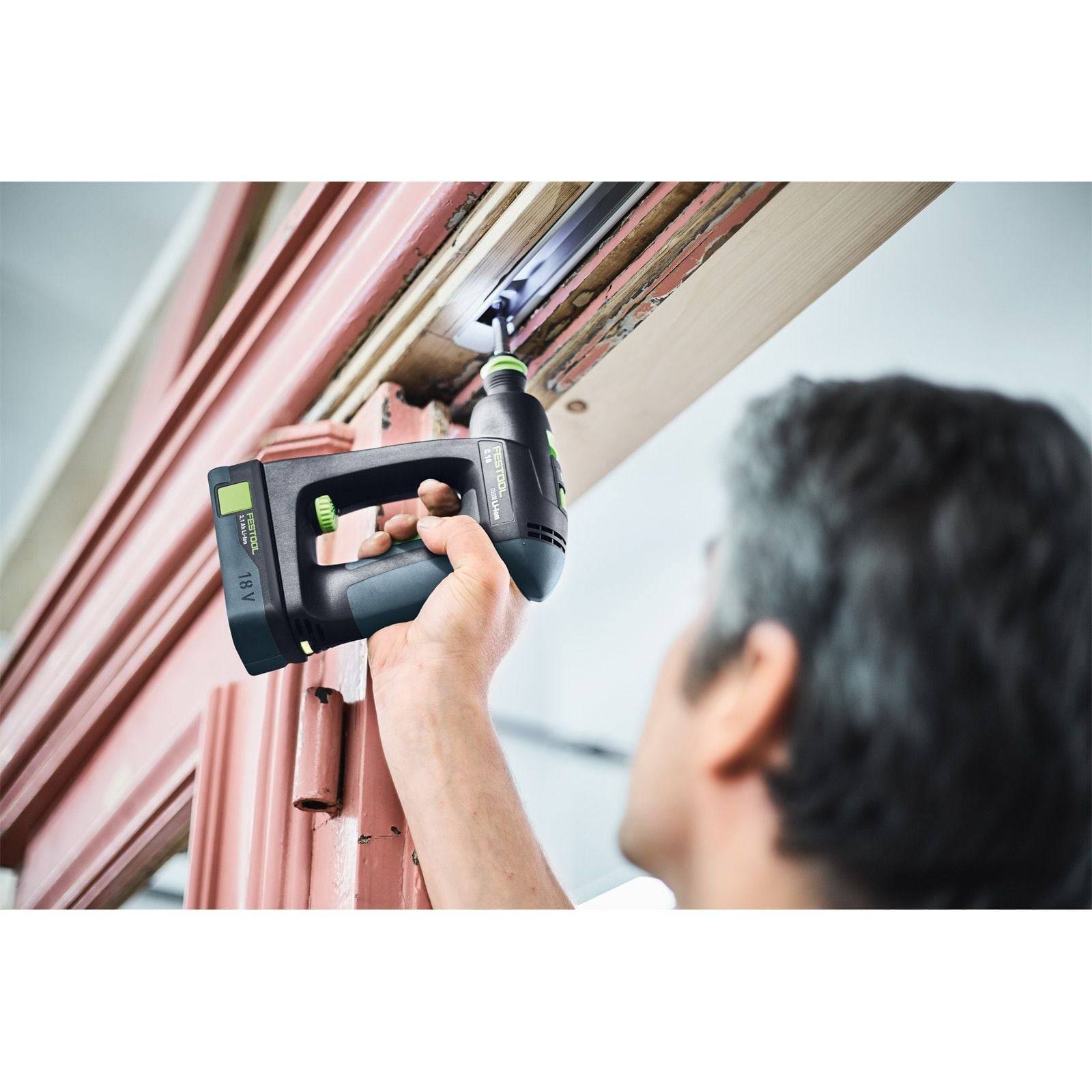 Eine Person, die einen schwarzen Akku-Bohrschrauber verwendet, um eine Schraube in einen Holztürrahmen drinnen zu befestigen oder zu entfernen. Der Fokus liegt auf dem Werkzeug und der ausgeführten Arbeit.